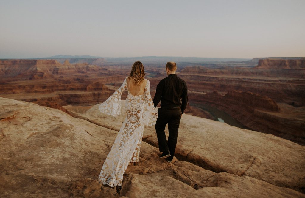 Bride and groom walk to cliff edge together in Dead Horse Point state park.