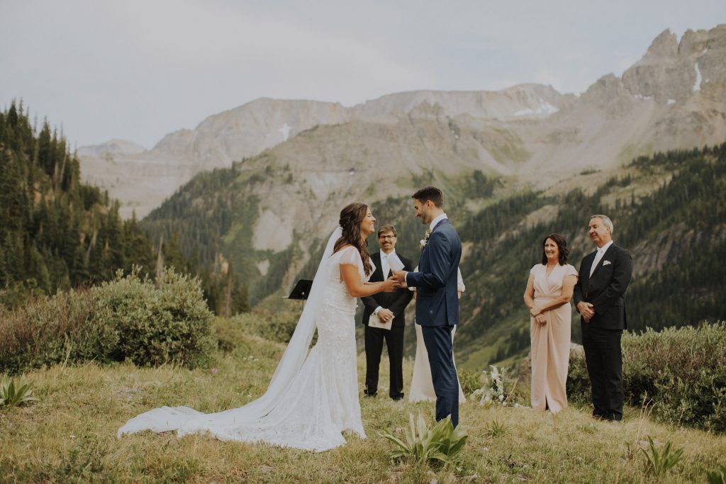 Couple holds hands, as they say their vows at Yankee Boy Basin, while their families watch.